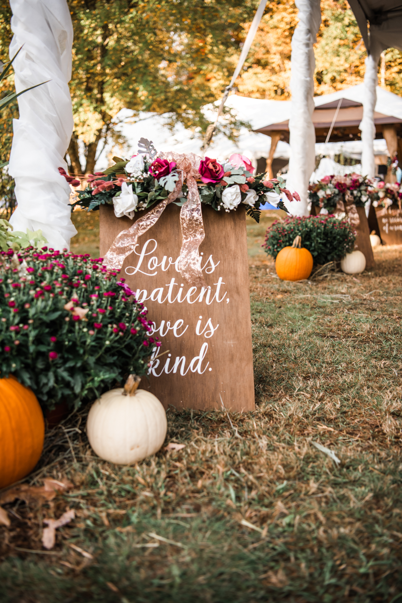 COVID wedding yard decor; wooden sign reading "Love is patient. Love is kind." surrounded by mums and pumpkins.